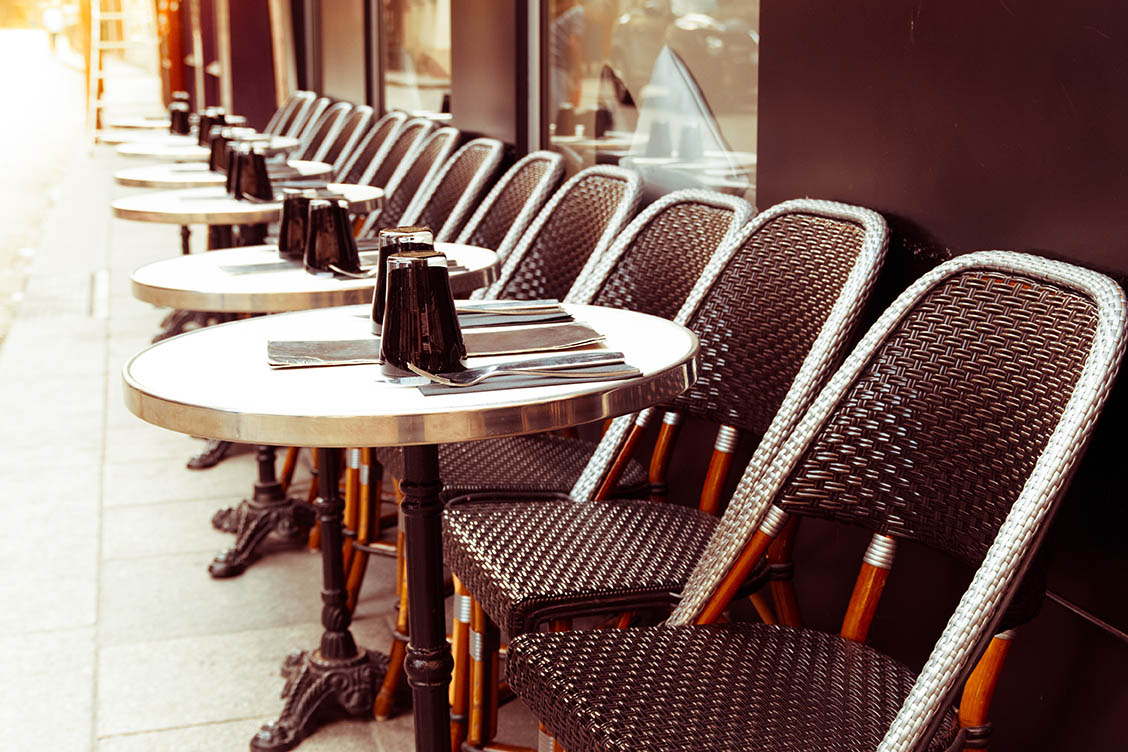 Outdoor seating area at a restaurant with brown chairs and small, round tables