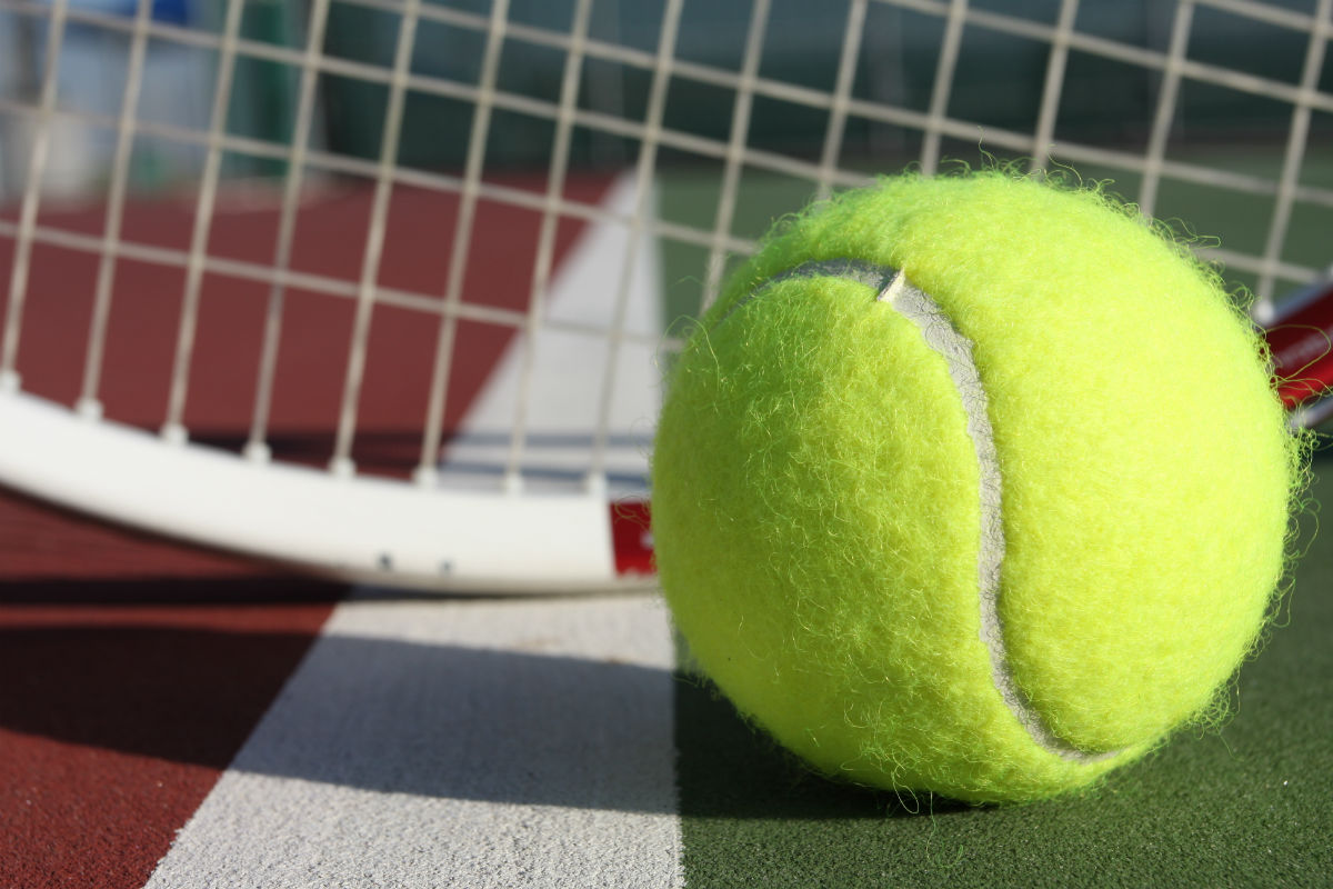 Tennis ball with a racket behind it on a tennis court